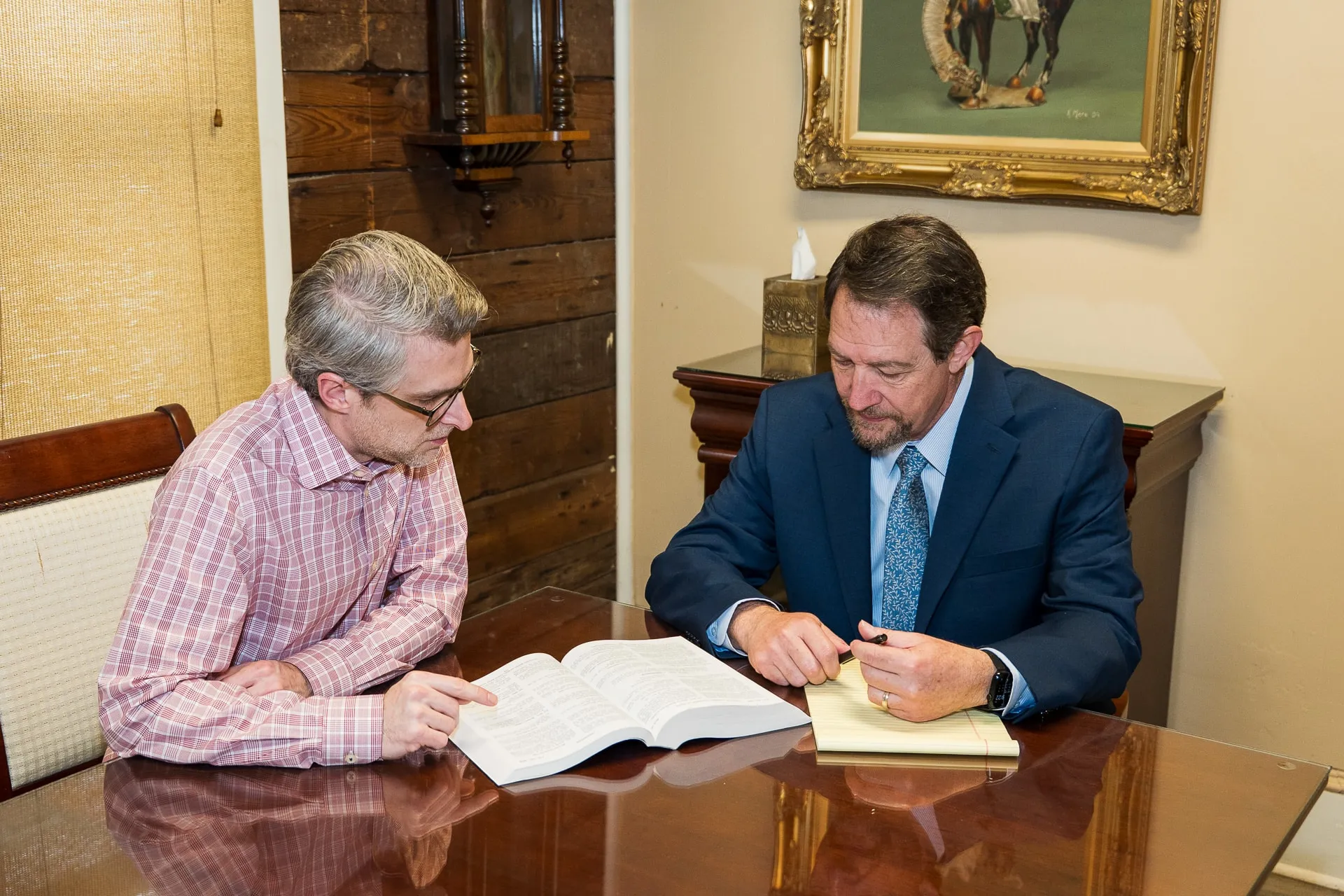 Richard D. Mere reviewing an open law book at his office table with a client seated beside him.