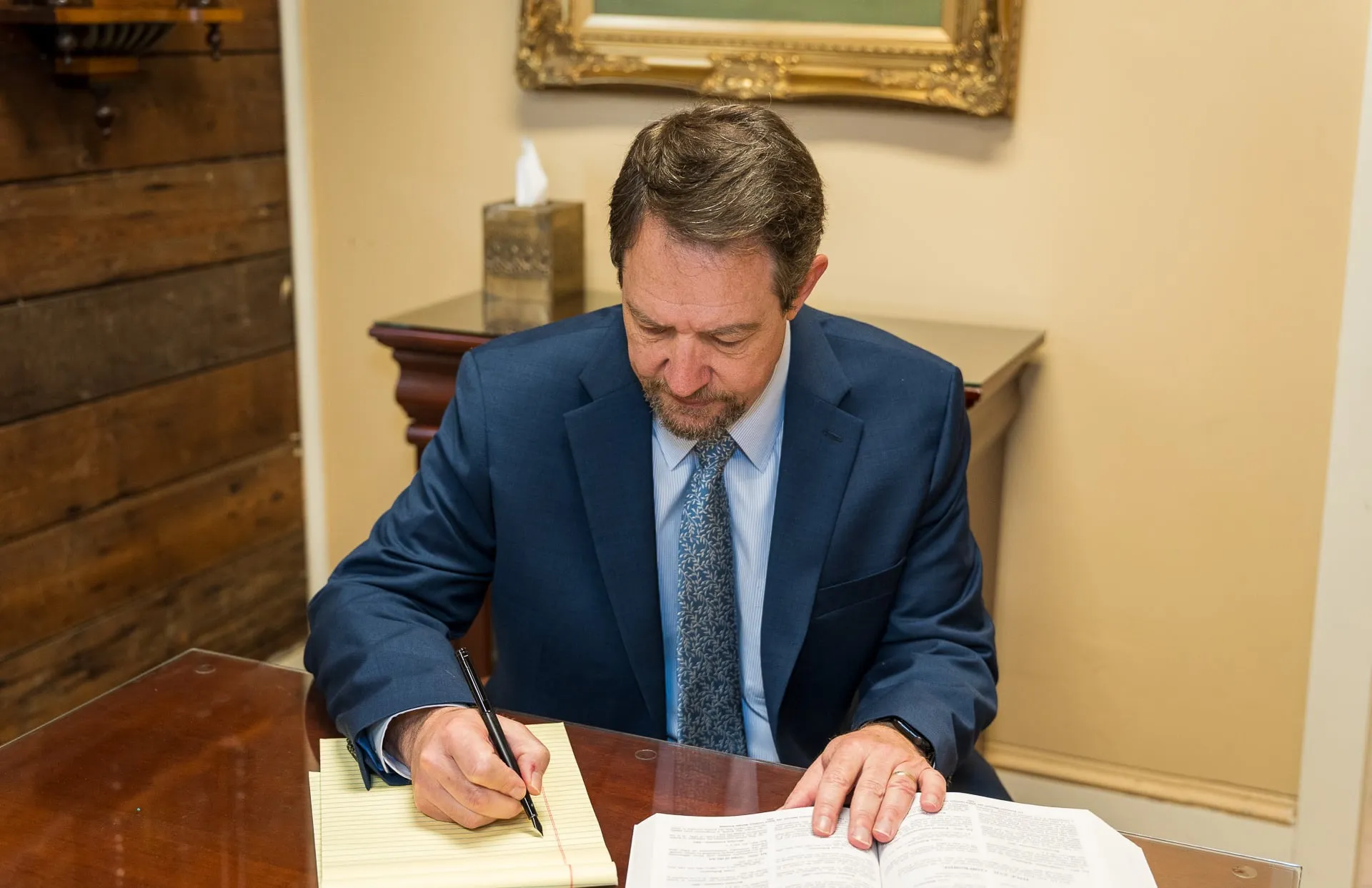 Richard D. Mere writing on a legal pad beside an open law book at his office table.